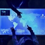 Mesa iluminada com mapa-múndi digital e pessoas apontando para diferentes regiões, simbolizando estratégias globais e expansão internacional.